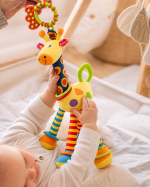 Bebé a brincar com peluche girafa colorido, com chocalho e argolas de dentição.