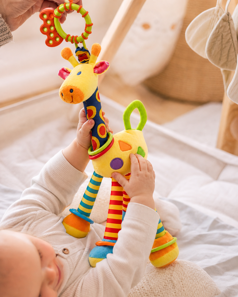Bebé a brincar com peluche girafa colorido, com chocalho e argolas de dentição.