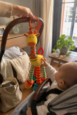 Peluche girafa de atividades com argolas coloridas pendurado num berço de bebé.