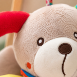 Pormenor da textura macia e detalhes do peluche de atividades em forma de cãozinho.