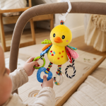 Bebé a brincar com o peluche passarinho de atividades pendurado no carrinho de passeio.