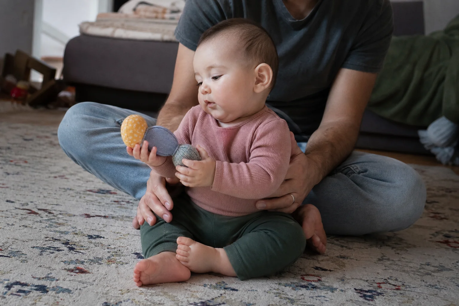 Bebé de seis meses apoiado por um adulto a explorar um brinquedo sensorial com as duas mãos